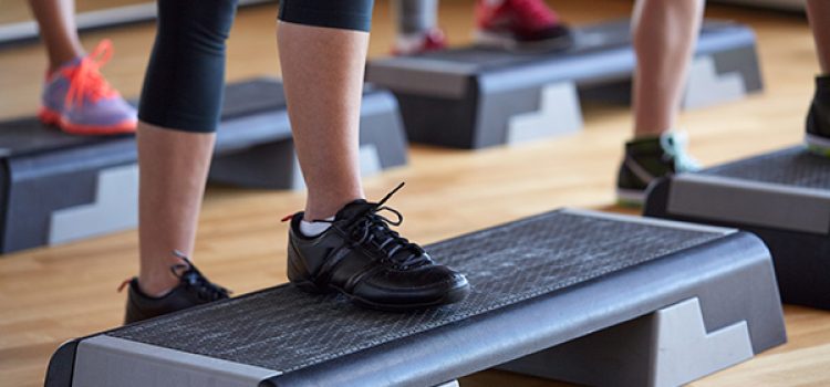 fitness, sport, people, step aerobics and lifestyle concept - close up of women legs exercising with steppers in gym