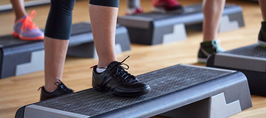 fitness, sport, people, step aerobics and lifestyle concept - close up of women legs exercising with steppers in gym