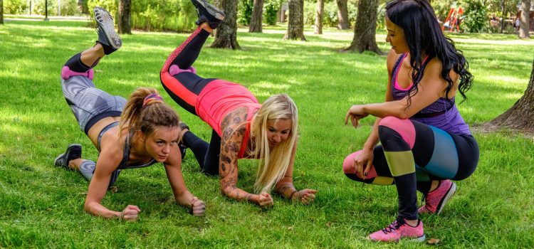 Three sporty females warming up in summer park.